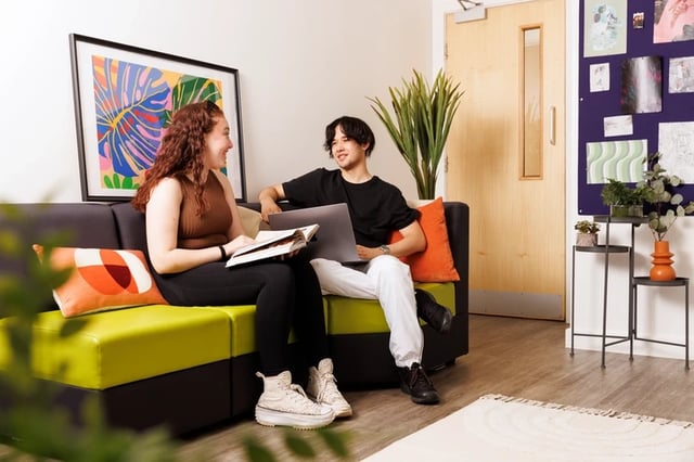 Two students on couch with laptop and book living room at Sir Charles Groves Hall in Manchester Student Accommodation