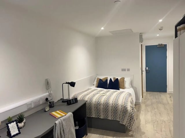 Desk lamp bed with blue pillows and patterned throw bedroom at Medici in Nottingham Student Accommodation