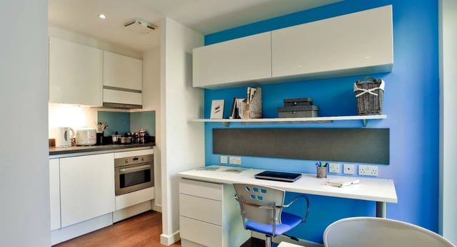 White cabinets desk chair and kitchen area study room at Griffon Studios in London Student Accommodation