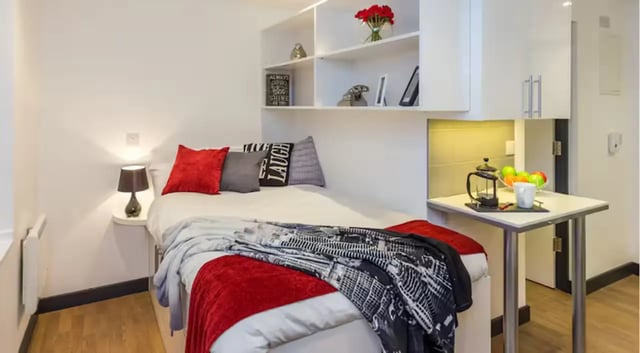 Bed with red blanket and pillows and small kitchen area Bedroom at The Court Yard in Southampton Student Accommodation