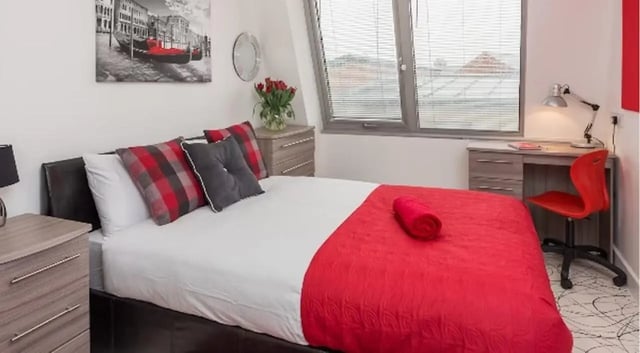 Bed with red accents desk chair and painting bedroom at Queens Gate in Southampton Student Accommodation