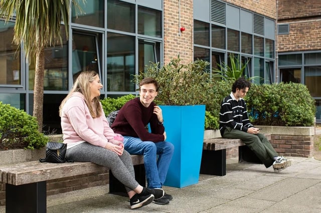 Students sitting on benches outside building exterior at Orion Point in Southampton Student Accommodation