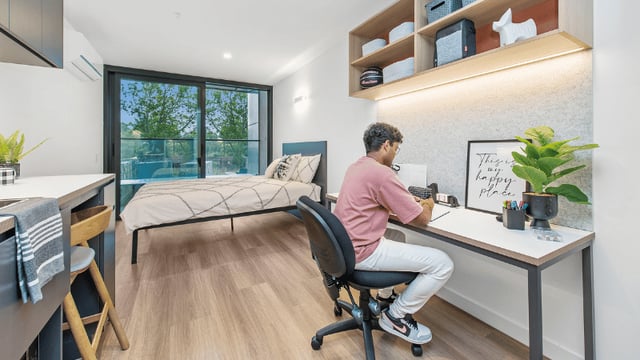 Student at desk with bed kitchen area bedroom at UniLodge Melbourne Flagstaff in Melbourne Student Accommodation