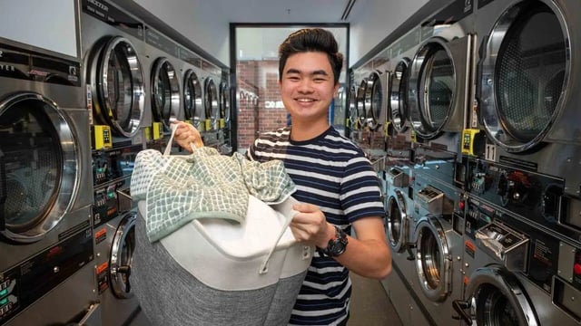 Man with laundry basket among washers and dryers laundry area at UniLodge Melbourne Central in Melbourne Student Accommodation