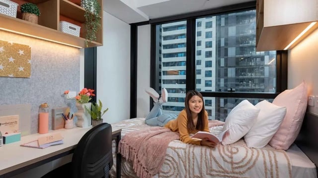 Woman on bed with desk and city view bedroom at UniLodge Melbourne Central in Melbourne Student Accommodation