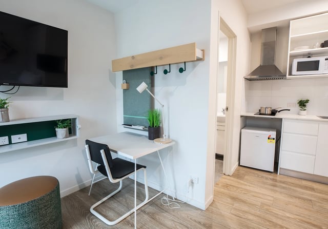 Desk chair plants TV shelf and kitchen area living room at UKO Stanmore in Sydney Student Accommodation