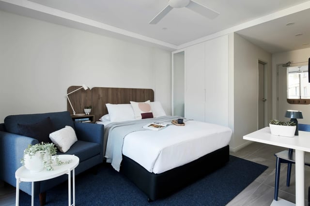 Blue armchair bed white bedding wooden headboard bedroom at UKO West Ryde in Sydney Student Accommodation