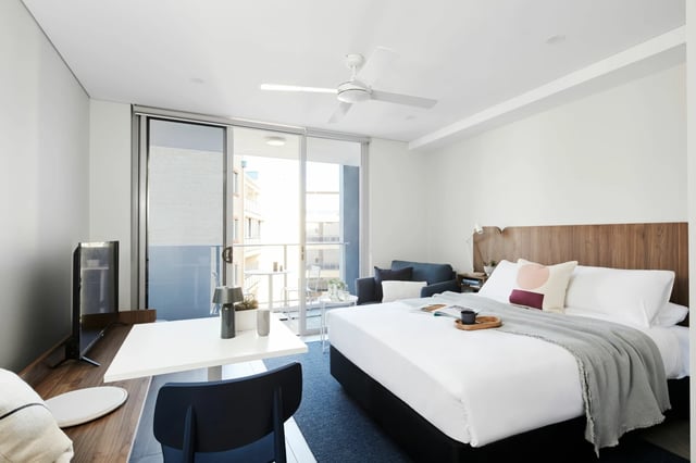 Bed desk chair sofa and balcony studio apartment at UKO West Ryde in Sydney Student Accommodation