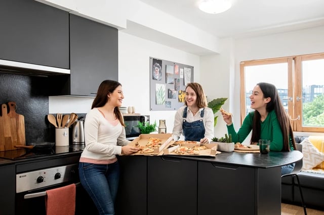 Three friends eating pizza in modern kitchen at Piccadilly Court in London Student Accommodation