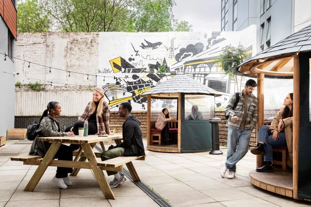 Students on picnic tables and pods exterior at Piccadilly Court in London Student Accommodation