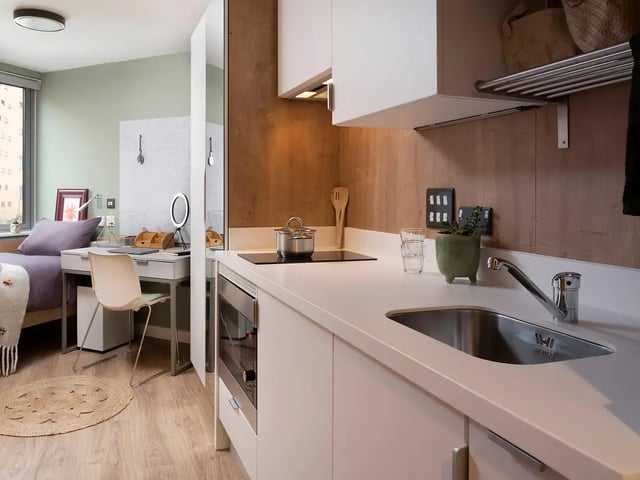 Bed desk chair and kitchen area living room at The Curve in London Student Accommodation