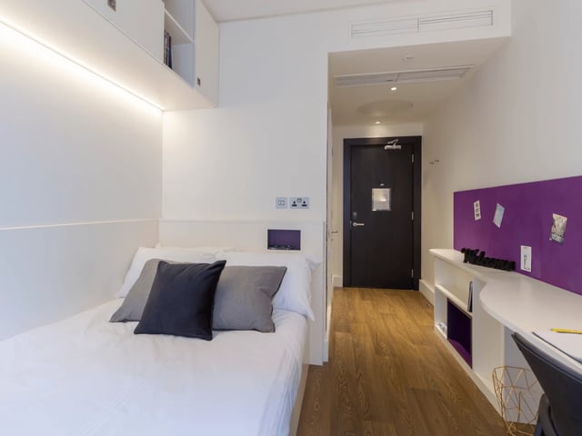 Bed with grey cushions and desk area bedroom at Spring Mews in London Student Accommodation