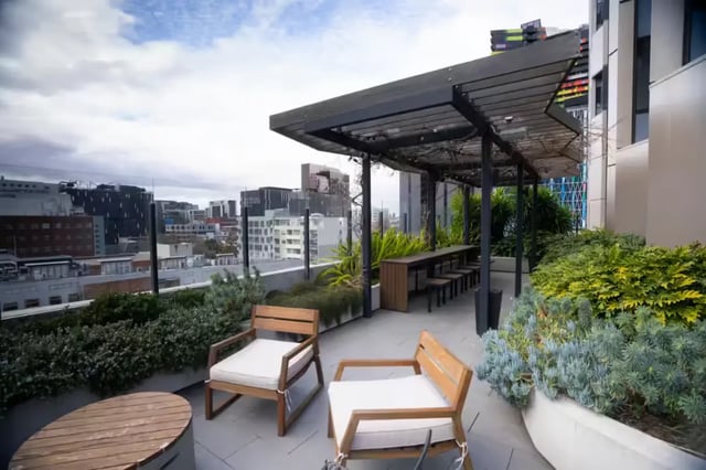 Wooden chairs table under pergola with city view outdoor area at Scape Uni Square in Melbourne Student Accommodation