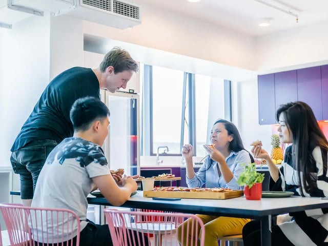 Students eating pizza at a table living room at Yugo Adelaide City in Adelaide Student Accommodation
