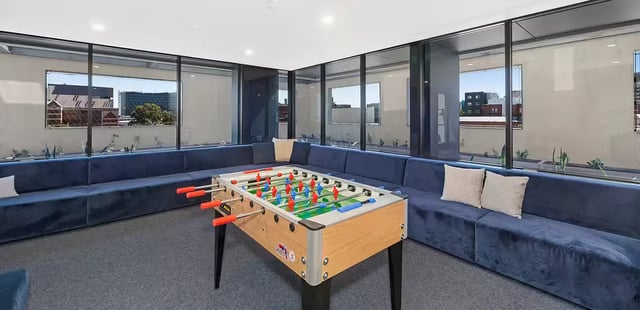 Foosball table on carpet with blue sectional seating area at Scape Waymouth in Adelaide Student Accommodation