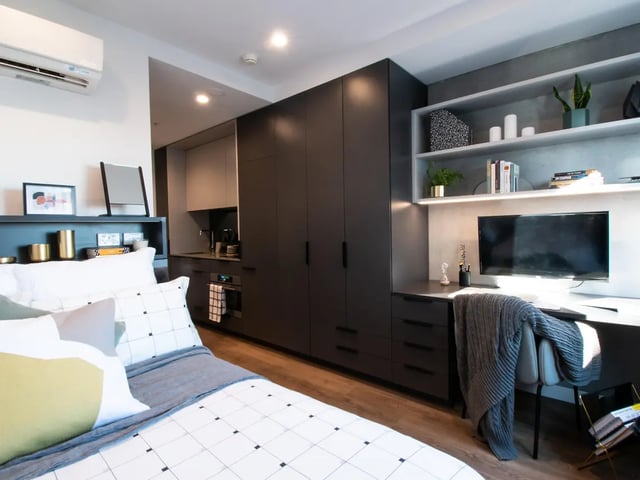 Bed desk wardrobe and kitchen studio apartment at Yugo University Square Melbourne in Melbourne Student Accommodation