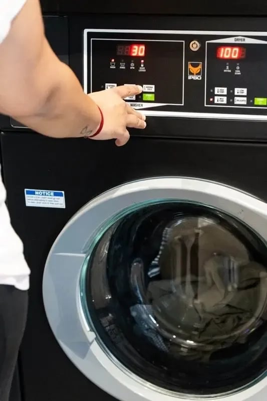 Hand presses button on washing machine Laundry room image at The Switch Adelaide in Adelaide Student Accommodation