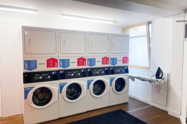 Stack of washing machines dryers ironing board laundry area at Don Gratton House in London Student Accommodation