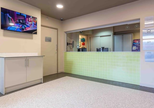 Reception desk with green tiles and computers reception area at iQ The Arcade in London Student Accommodation