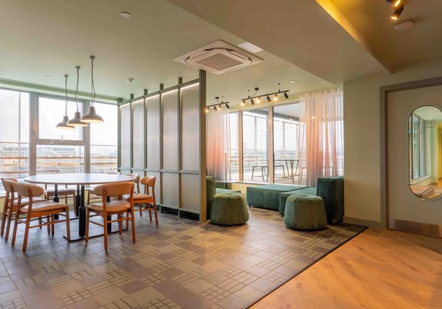 Dining table chairs green ottomans sofas lounge area at iQ Paris Gardens in London Student Accommodation