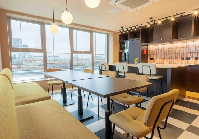Large table yellow bench bar stools kitchen area living room at iQ Paris Gardens in London Student Accommodation