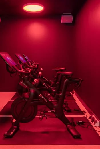 Spin bikes with screens under red lighting gym at ARK Wembley in London Student Accommodation
