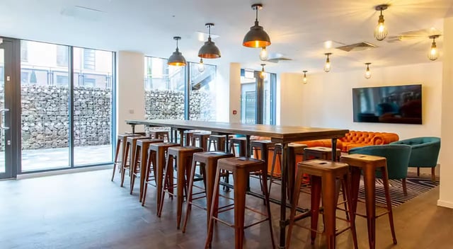 Long table stools orange sofa teal chairs living room at Dean Street Works in Bristol Student Accommodation