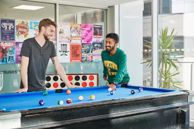 Two men playing pool with posters living room at Scape Adelaide Central in Adelaide Student Accommodation