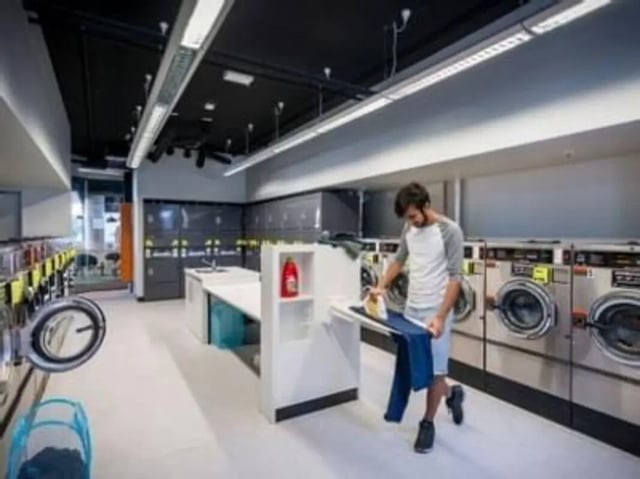 Man ironing clothes by washing machines laundry area at Unilodge South Bank in Brisbane Student Accommodation