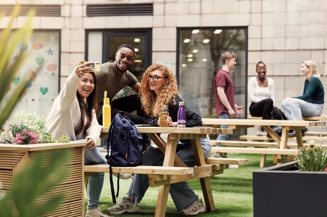 Students taking selfie at picnic table exterior area at Grand Central in Liverpool Student Accommodation