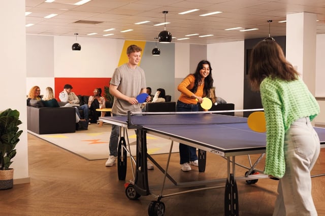 Students playing ping pong with lounge area in background playing area at Grand Central in Liverpool Student Accommodation