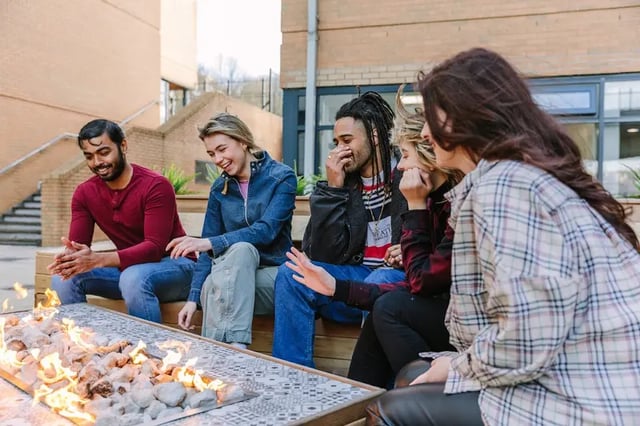 Students laughing around outdoor fire pit exterior at The Pinnacles in Sheffield Student Accommodation