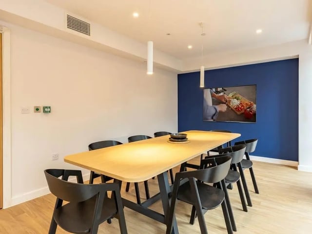 Long table with chairs TV on blue wall communal area at Straits Aire in Leeds Student Accommodation