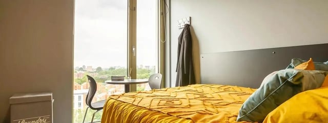 Bed with yellow bedding table chairs window bedroom at Element Manchester in Manchester Student Accommodation