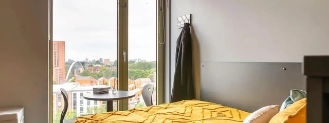Bed with yellow throw and table bedroom. at Element Manchester in Manchester Student Accommodation