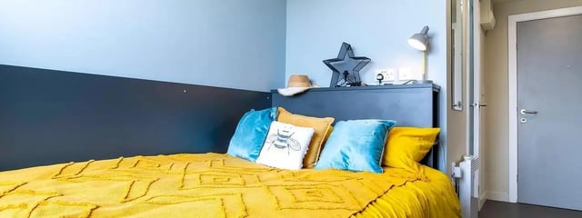 Bed with yellow bedding blue pillows and star lamp bedroom at Element Manchester in Manchester Student Accommodation