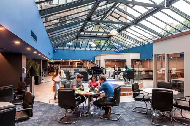 Students study around tables with piano living area at Study Inn Talbot Street Nottingham in Nottingham Student Accommodation