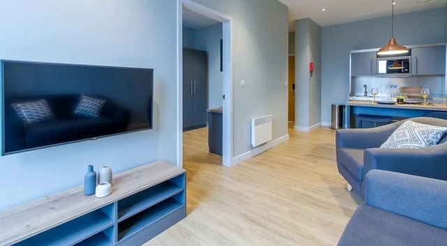 TV on wall with sofa behind and kitchen area living room at Crown House in Sheffield Student Accommodation