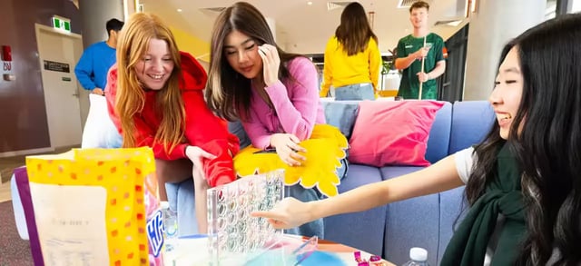 Students playing connect four on sofa Living area at Scape Lachlan in Sydney Student Accommodation