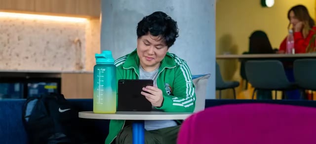 Man using tablet and water bottle common area at Scape Lachlan in Sydney Student Accommodation