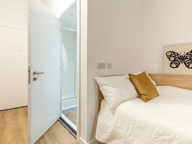 Bed with white linens golden pillow doorway to shower bedroom at Beckton House in Nottingham Student Accommodation