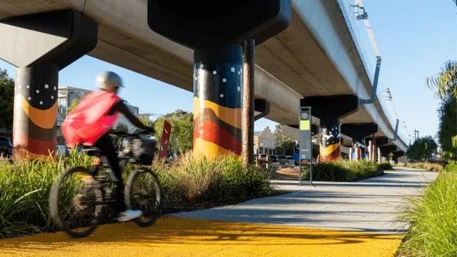 Person cycling under bridge with painted pillars exterior at WeAreLiving Preston in Melbourne Student Accommodation