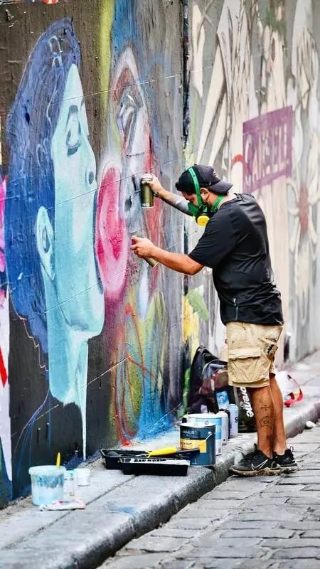 Graffiti artist sprays mural paints exterior art piece at Indi Footscray in Melbourne Student Accommodation