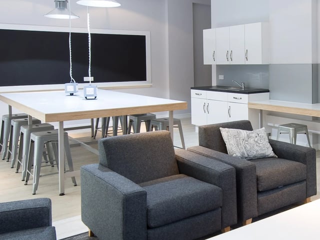 Dark grey armchairs table with stools kitchen area living room at Glassyard Building in London Student Accommodation