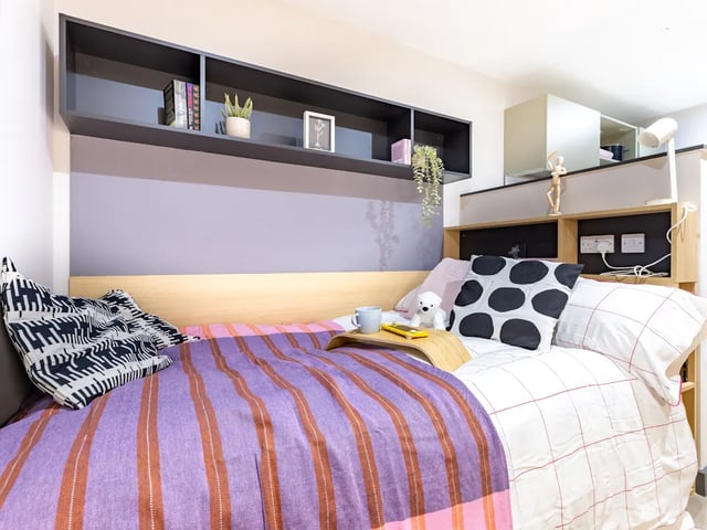 Bed with striped throw shelf with books teddy bear Bedroom at Biscuit Factory in Belfast Student Accommodation