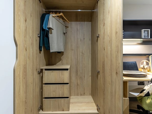 Open wooden wardrobe with clothes and drawers bedroom area at Biscuit Factory in Belfast Student Accommodation