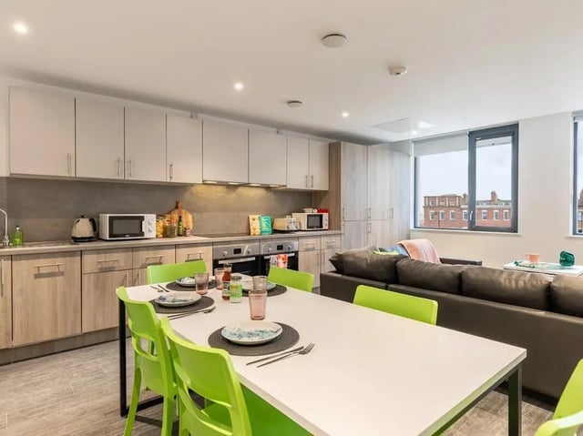 Dining table with green chairs and kitchen living room. at Glassworks in Bristol Student Accommodation