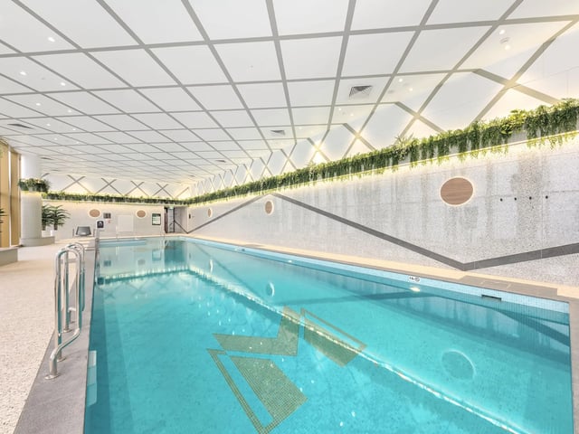 Indoor swimming pool with bright turquoise water and mosaic geometric pattern playing area at Belong Macquarie in Sydney Student Accommodation