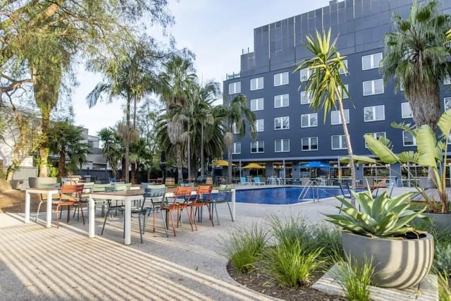 Outdoor dining tables pool lounge chairs and building exterior at Campus Melbourne in Melbourne Student Accommodation