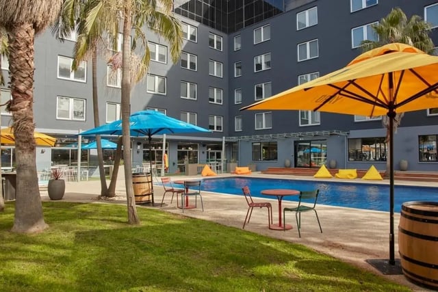 Palm trees pool umbrellas seating and barrel outdoor area at Campus Melbourne in Melbourne Student Accommodation